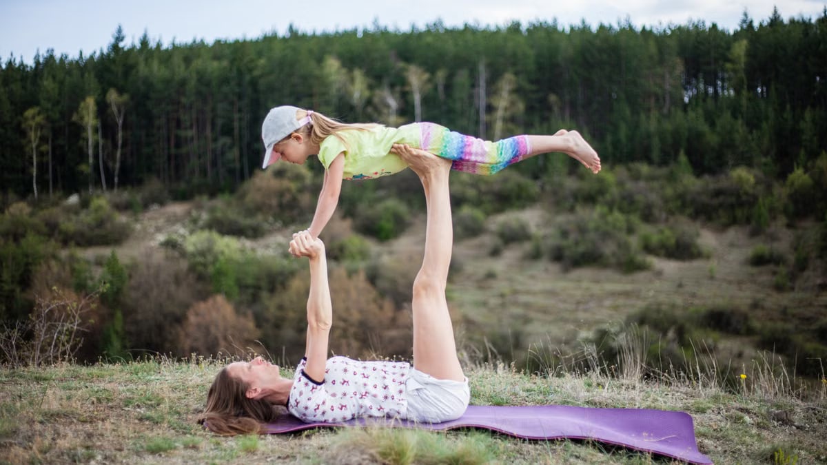 Mother and daughter enjoy a playful acro yoga session on a grassy hilltop, strengthening their bond.